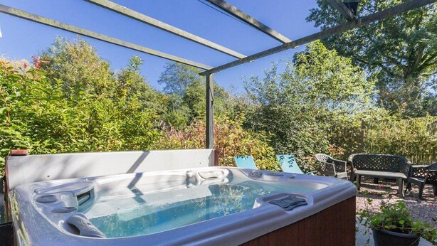 Ein Whirlpool unter einer Holzpergola mit Blick auf Bäume und einer Terrasse mit Sitzgelegenheiten.