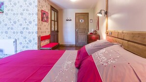 Ein Schlafzimmer mit einem Bett, einem hölzernen Kopfteil, einem roten Sessel, einer Holztür und einer Wand mit einem Blumenmuster.