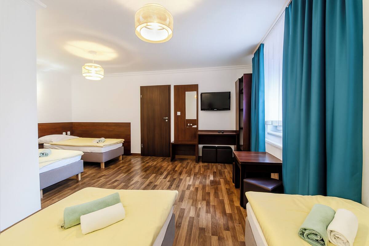 A hotel room with two beds, a desk, a TV, and a large window with curtains.