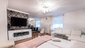 A modern hotel room with a flat-screen TV mounted on the wall, a sofa, a bed with a pink throw, and a glass coffee table. - Noclegi Europa (Boleslawiec)