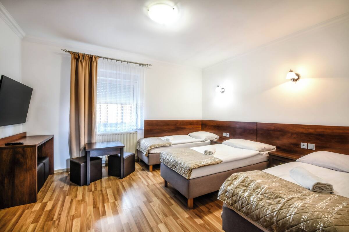 A hotel room with two beds, a wooden floor, a TV, and a window with curtains.