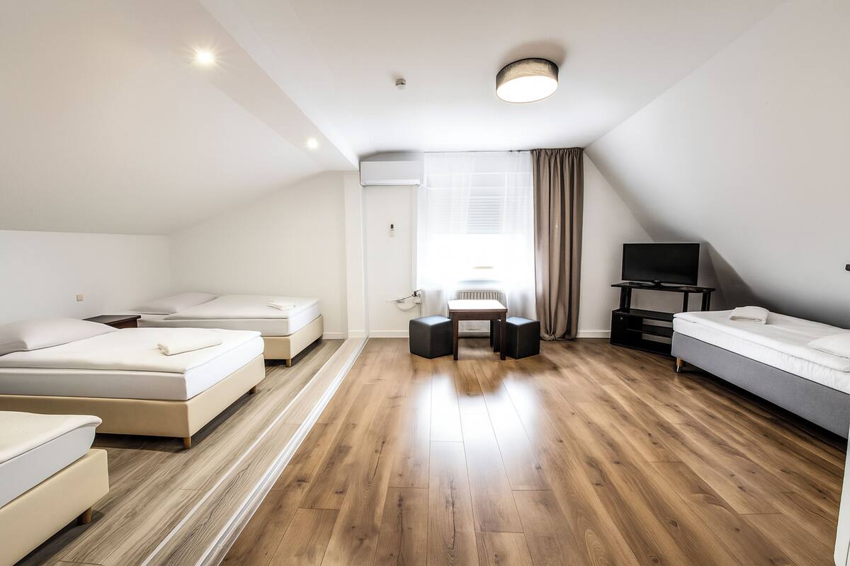 A modern, well-lit room with two single beds, a small table, a TV, and a window with curtains.