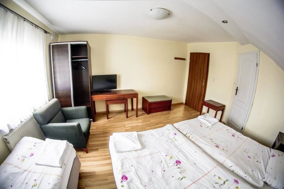 A hotel room with a bed, a sofa, a desk with a TV, a wardrobe, and a small table.