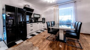 A modern kitchen with a black refrigerator, microwave, and stove, a dining table with black chairs, and a large window with curtains. - Noclegi Europa (Boleslawiec)