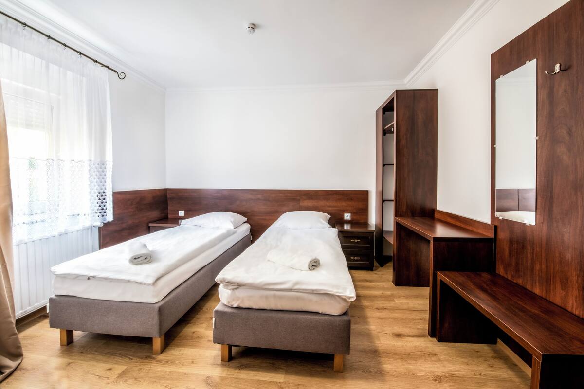 A hotel room with two single beds, a wooden bench, a mirror, and a wardrobe.