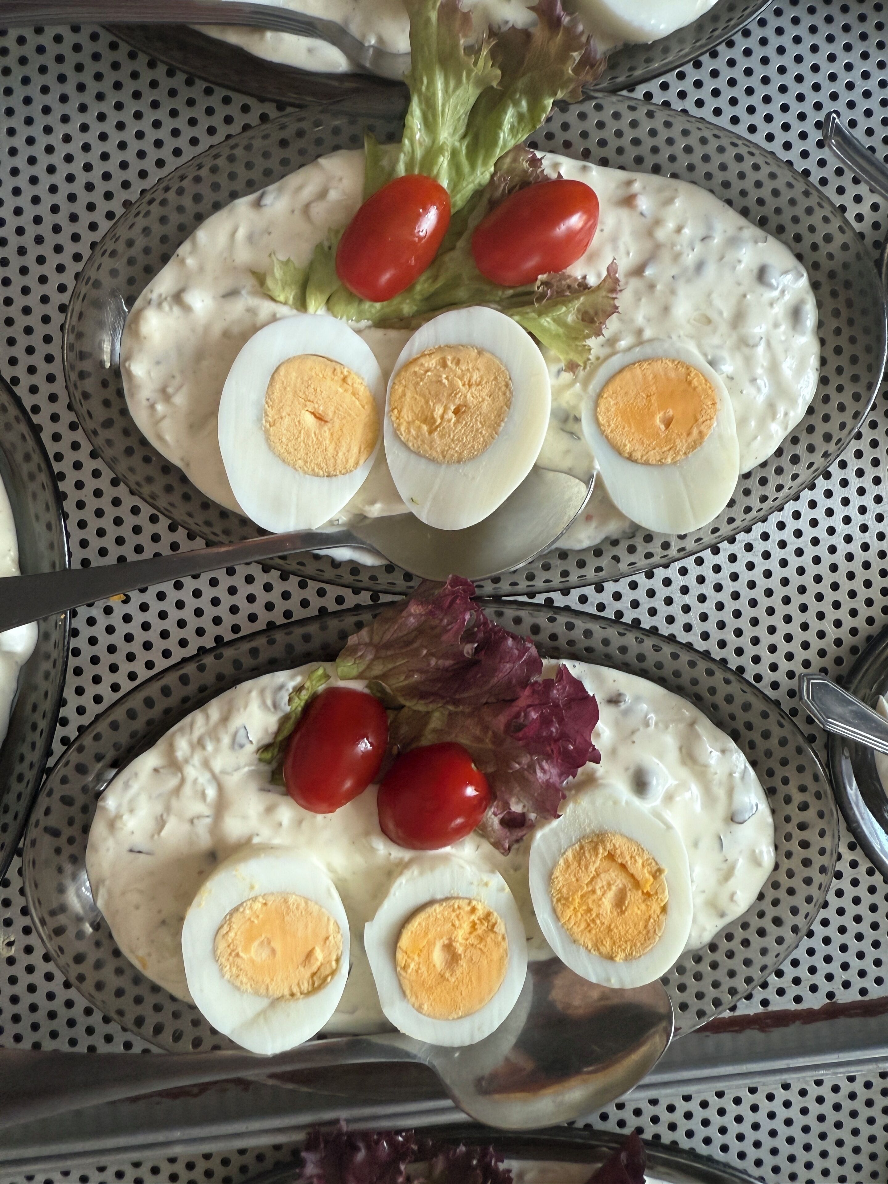 A salad with hard-boiled eggs and cherry tomatoes on a perforated metal tray.