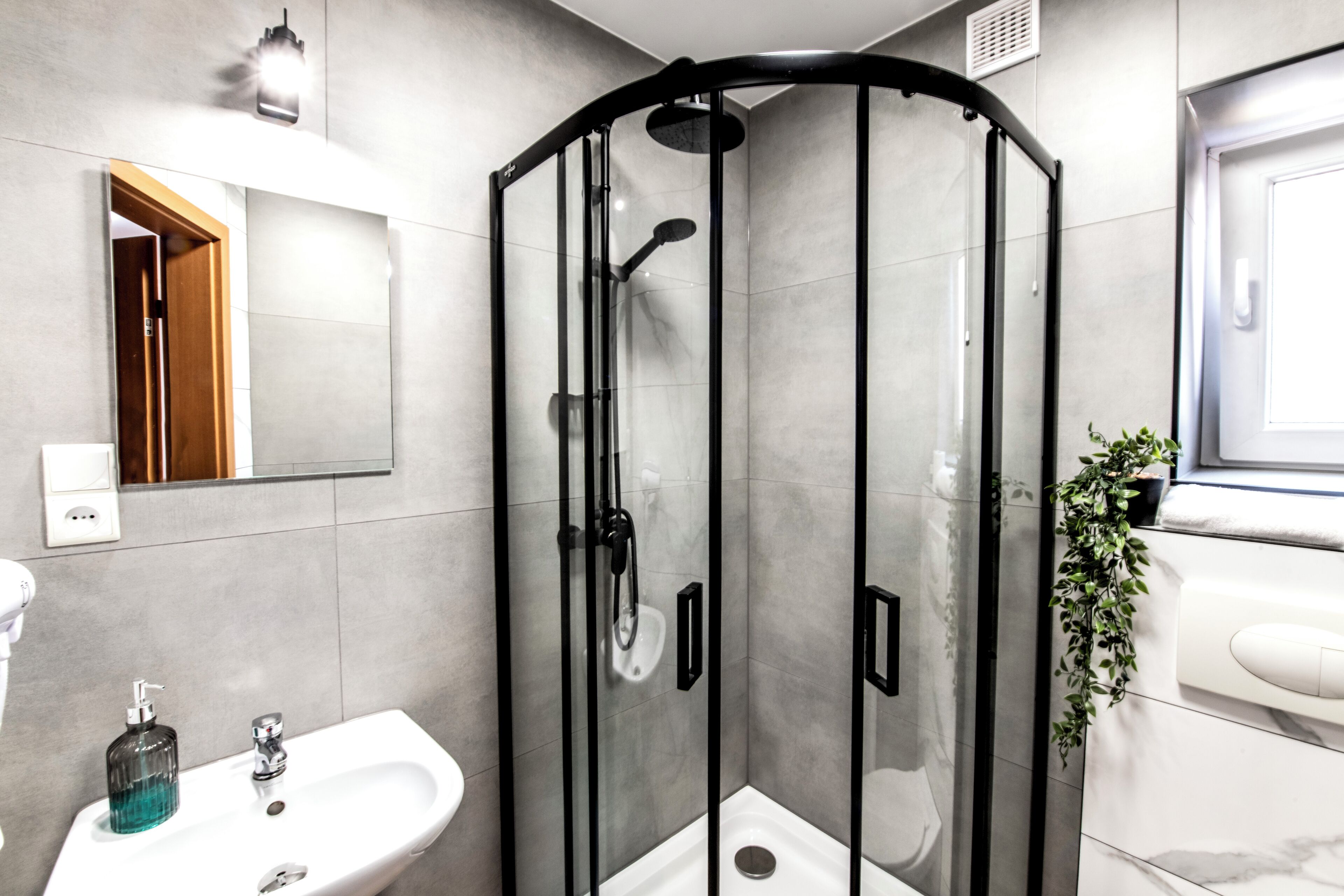 A modern bathroom with a glass-enclosed shower, a sink with a soap dispenser, and a mirror above the sink.