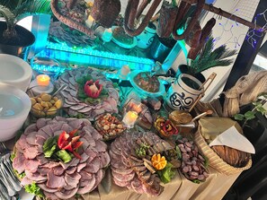 Una mesa con diversos alimentos, como embutidos, quesos y verduras, sobre un mantel.