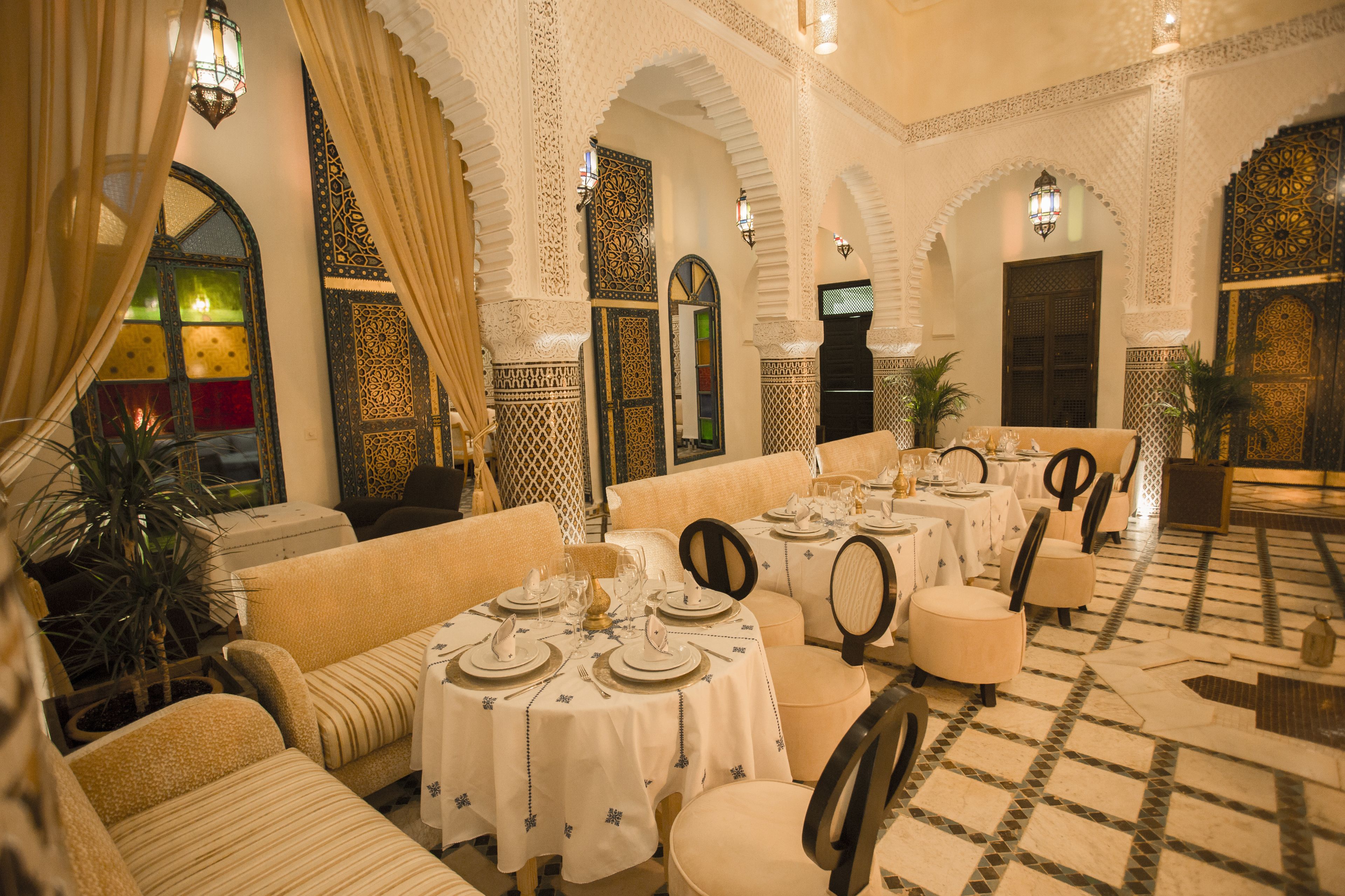 A dining area with tables set for guests, featuring ornate wall designs and a patterned floor.