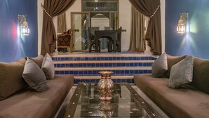 A room with a sofa, a glass coffee table with a decorative vase, and a view of a staircase leading to a balcony. - Palais Dar Si Aissa ALL-SUITES (Marrakech)