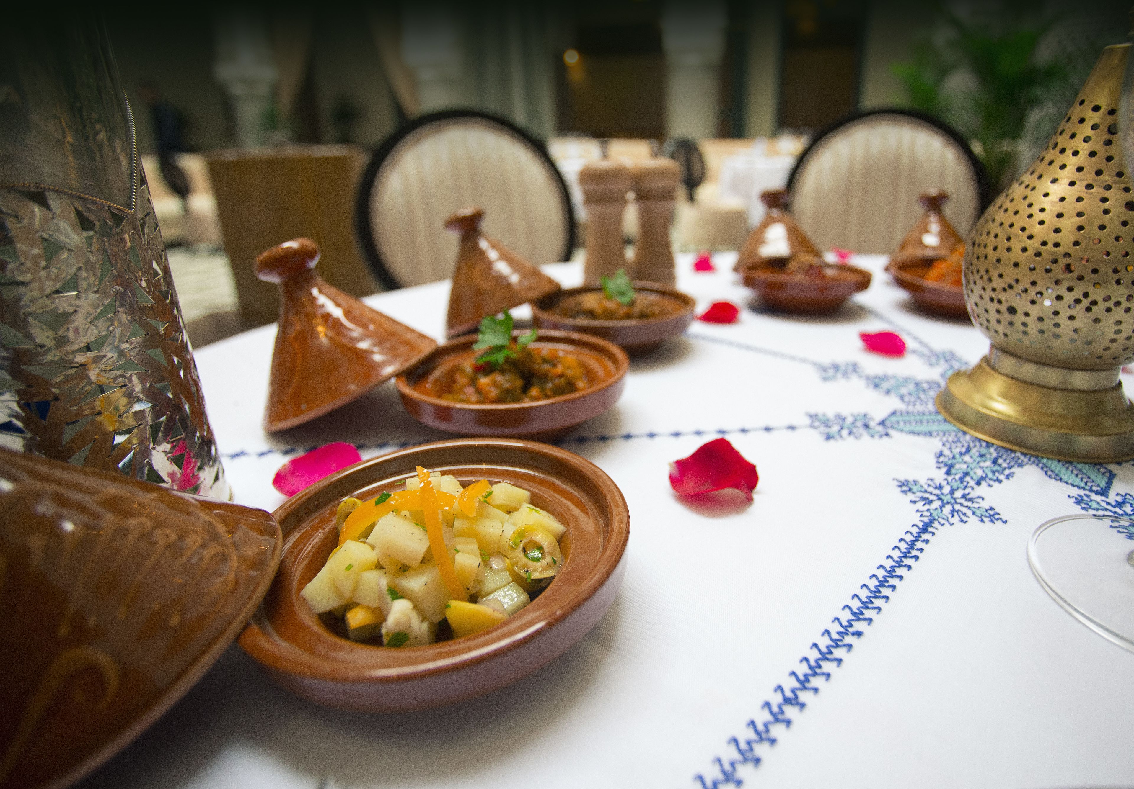 Une table à manger ornée de plats traditionnels marocains, d’une lampe en laiton et d’un vase décoratif.