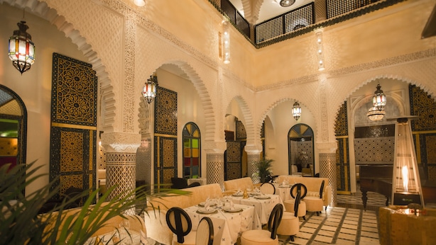 A traditional Moroccan interior with ornate arches, patterned walls, and a central dining area with tables and chairs. - Palais Dar Si Aissa ALL-SUITES (Marrakech)