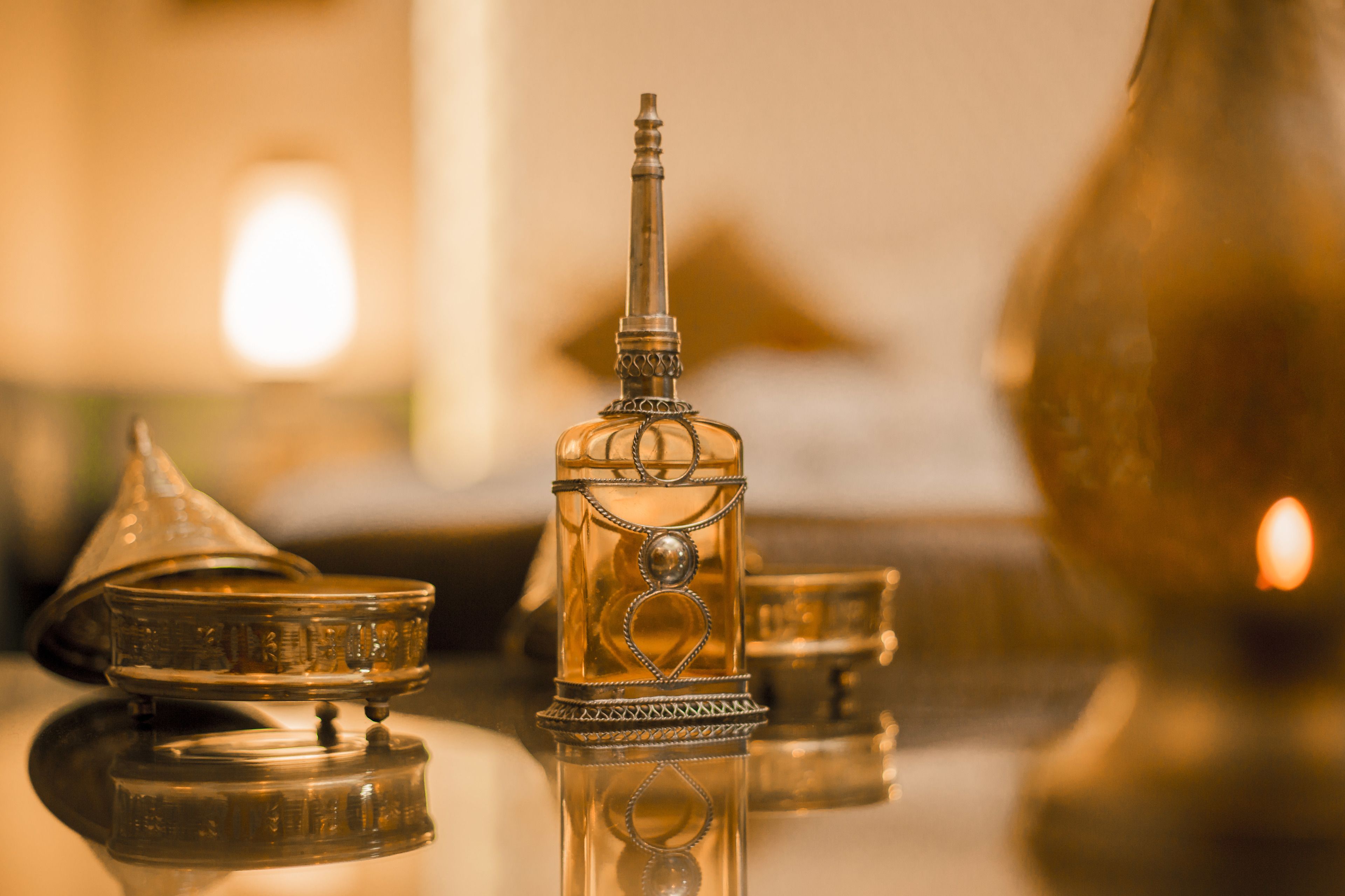A close-up of a traditional brass teapot with intricate designs, accompanied by a matching cup and saucer, reflecting on a polished surface.
