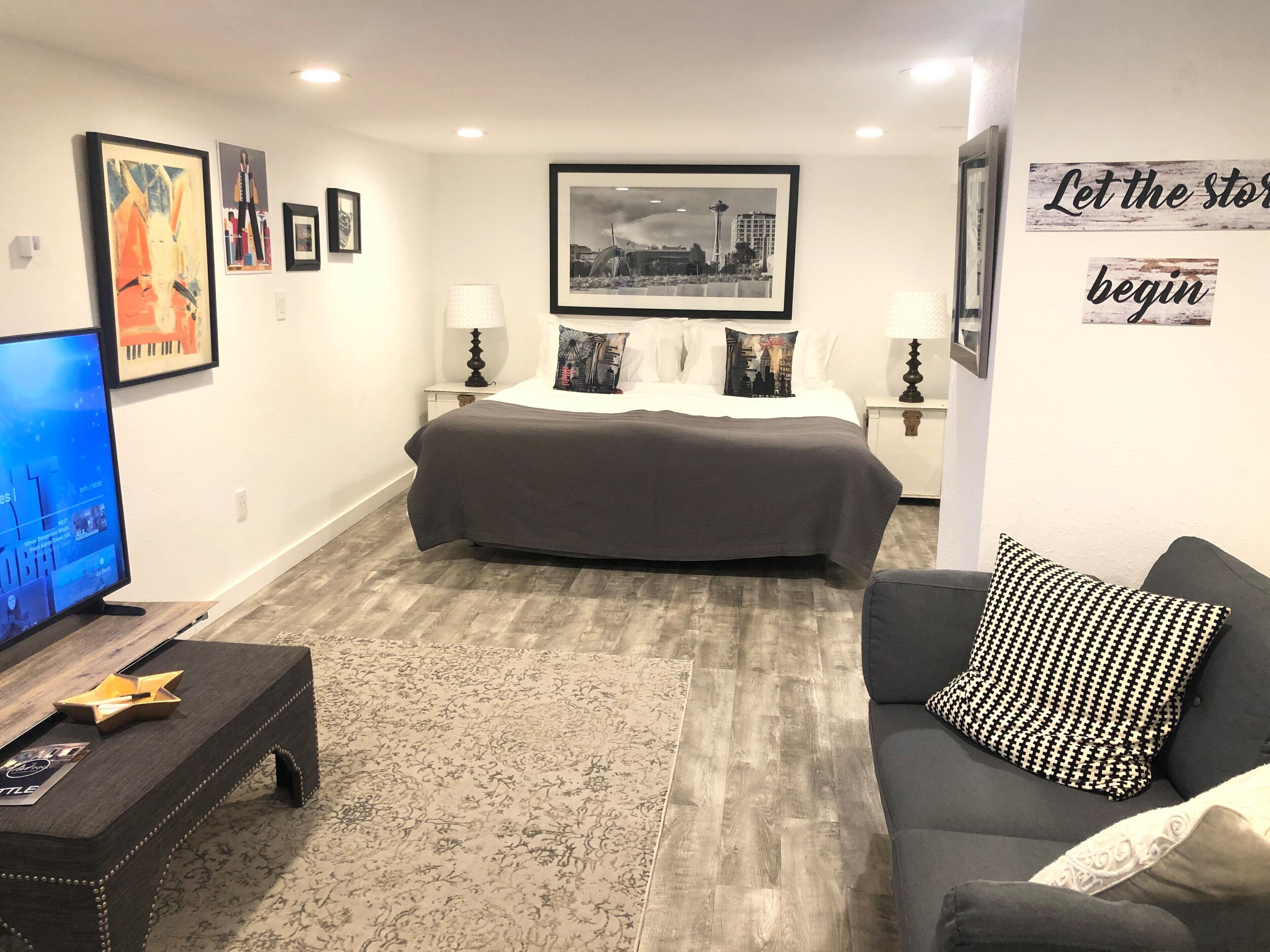 A modern hotel room with a large bed, a TV, a sofa, and artwork on the walls.
