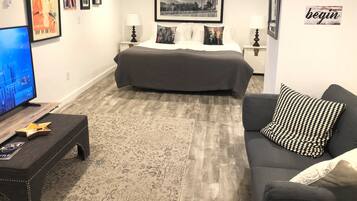 A modern hotel room with a large bed, a TV, a sofa, and artwork on the walls.