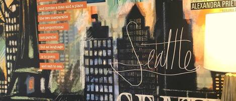 A room with a Seattle-themed wall mural, a bed with a pillow, and a lamp.