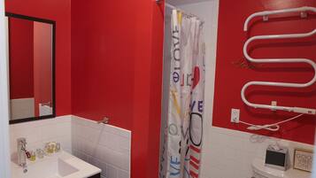 A bathroom with a red wall, a white sink, a mirror, a shower curtain with 'LOVE' text, and a towel rack.