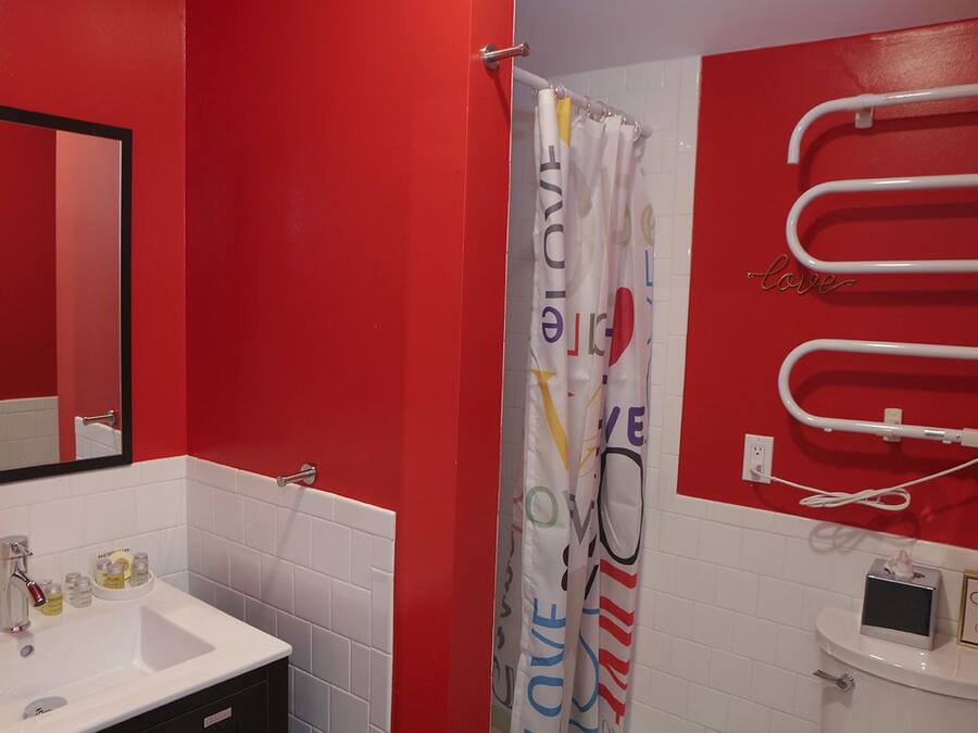 A bathroom with a red wall, a white sink, a mirror, a shower curtain with 'LOVE' text, and a towel rack.
