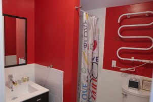 A bathroom with a red wall, a white sink, a mirror, a shower curtain with 'LOVE' text, and a towel rack.