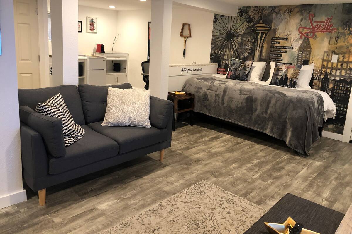 A modern bedroom with a bed, a sofa, and a city-themed wall mural.