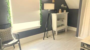 A room with a white chair, a floor lamp, and a white shelf unit against a dark wall.