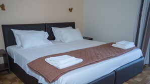 A neatly made bed with white linens and a brown quilted blanket, a dark headboard, and a wooden floor. - Hotel Milton (East Mani)