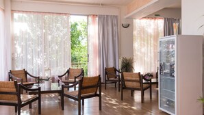 A spacious room with a dining area featuring wooden chairs and a glass table, a refrigerator, and large windows with curtains. - Hotel Milton (East Mani)