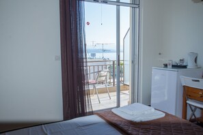 A hotel room with a bed, a small kitchenette, a balcony with a chair, and a view of the sea. - Hotel Milton (East Mani)