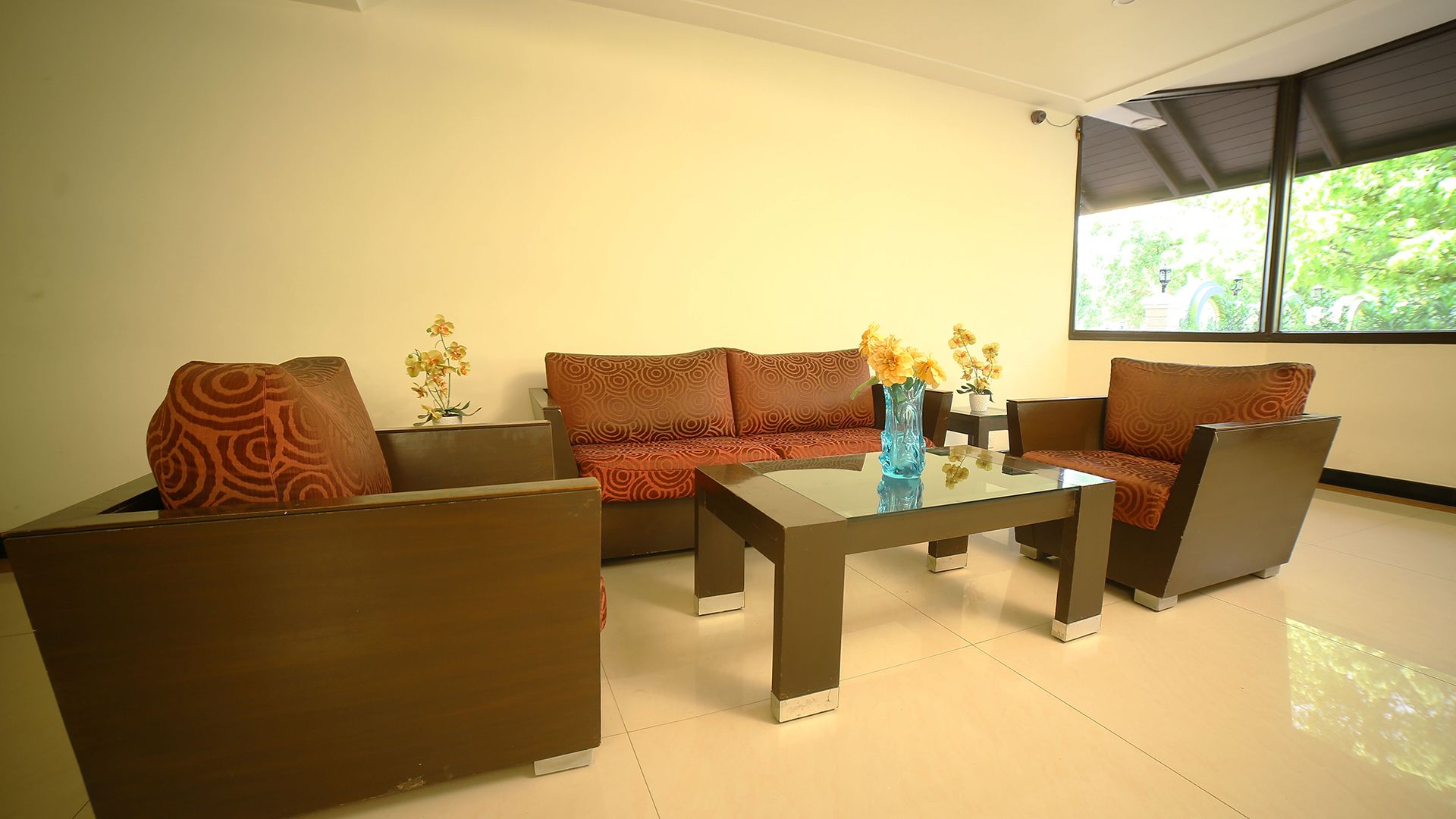 Una sala de estar moderna con un sofá, sillones y una mesa de centro de vidrio. Hay jarrones con flores sobre la mesa.