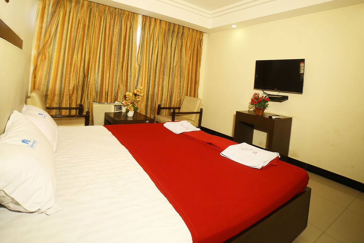 A hotel room with a bed, a desk, a chair, a TV, and curtains.