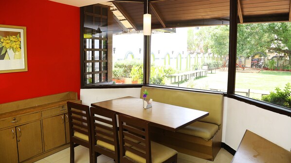A small kitchen with a table and chairs, a window with a view of a garden, and a red wall.