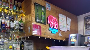 A bar area with a martini glass on a counter, various liquor bottles, and a neon sign. - Village vacances Cévéo du Haut Breda (Le Haut-Bréda)