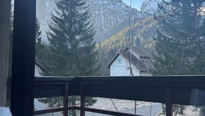 A room with a view of snow-covered mountains, a wooden deck, and a window overlooking a house. - Village vacances Cévéo du Haut Breda (Le Haut-Bréda)