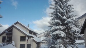 A snow-covered residential area with houses, a large snow-laden tree, and a mountain in the background. - Village vacances Cévéo du Haut Breda (Le Haut-Bréda)