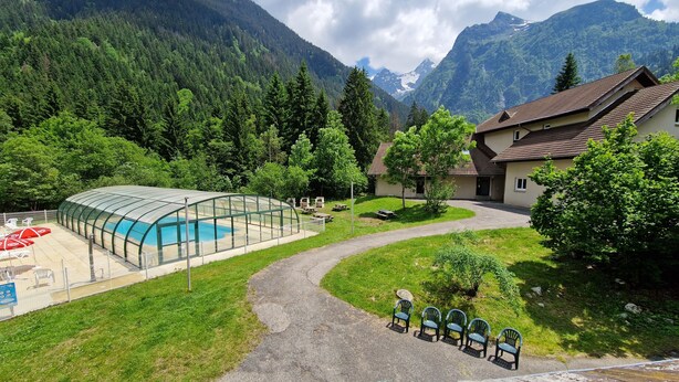 A pool with a glass enclosure, a pathway, and a building with a sloped roof. - Village vacances Cévéo du Haut Breda (Le Haut-Bréda)