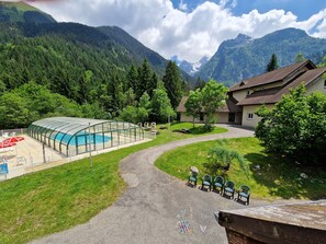 Una piscina con cerramiento de vidrio, un sendero y un edificio de techo inclinado.