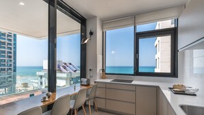 A modern kitchen with a large window overlooking the sea, a dining area with chairs, and a small island with a sink. - Front of Beach next to RoyalBeach Hotel (Tel Aviv)