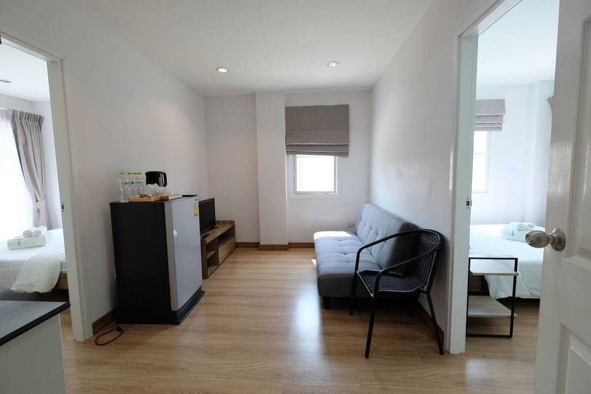 A compact hotel room with a kitchenette, a sofa, a dining table, and a bed.