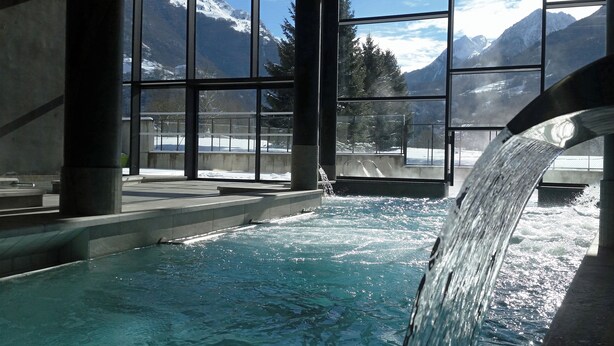 A pool with a waterfall feature, large windows with a mountain view, and a concrete structure. - Village Cévéo de Luz-Saint-Sauveur (Luz-Saint-Sauveur)
