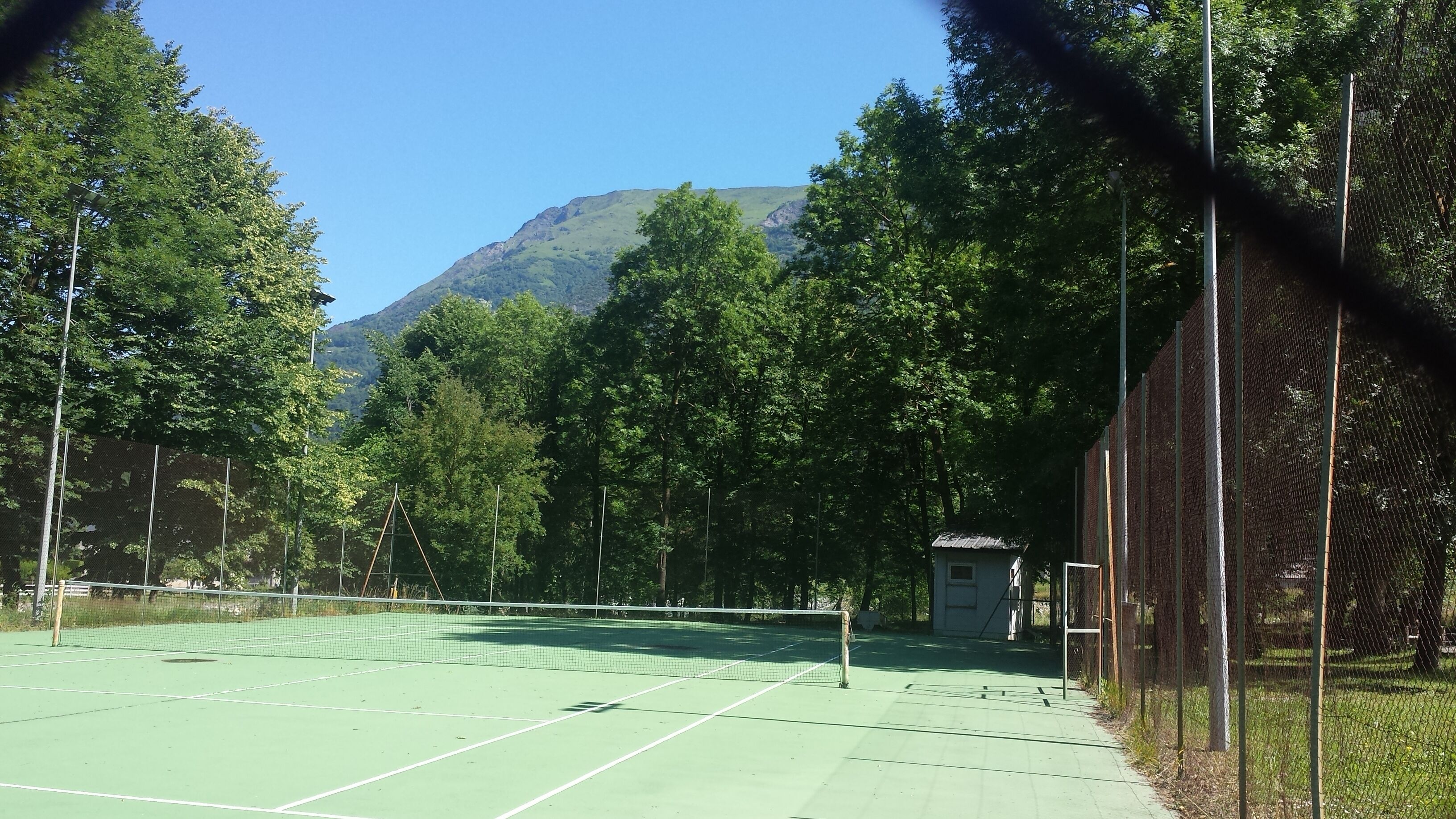 A tennis court surrounded by trees and a mountain in the background.
