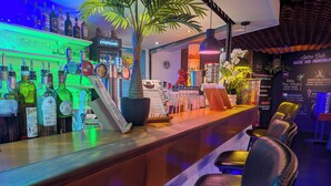 A bar area with a counter, bar stools, a neon sign, and a menu board. - Village Cévéo de Luz-Saint-Sauveur (Luz-Saint-Sauveur)