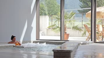 Une personne se trouve dans un bain à remous, avec vue sur un espace extérieur aménagé avec des chaises et un parasol en chaume.