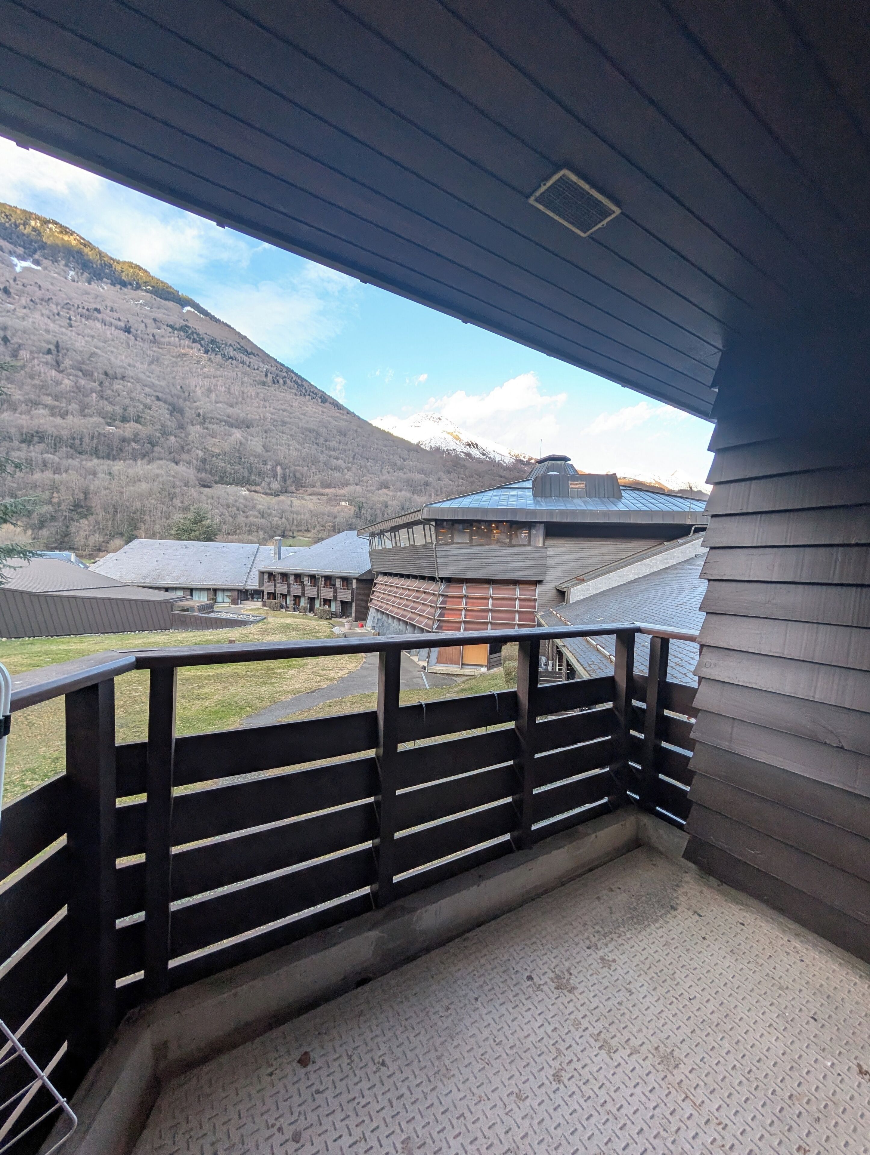 A balcony with a metal railing overlooking a mountainous landscape and a building with a sloped roof.