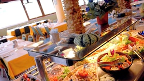 A buffet with various food items, a glass display case, and a seating area with tables and chairs. - Village Cévéo de Luz-Saint-Sauveur (Luz-Saint-Sauveur)