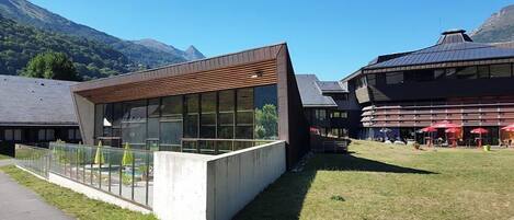 Um edifício moderno com grandes janelas, estrutura de concreto e área gramada com mesas ao ar livre.