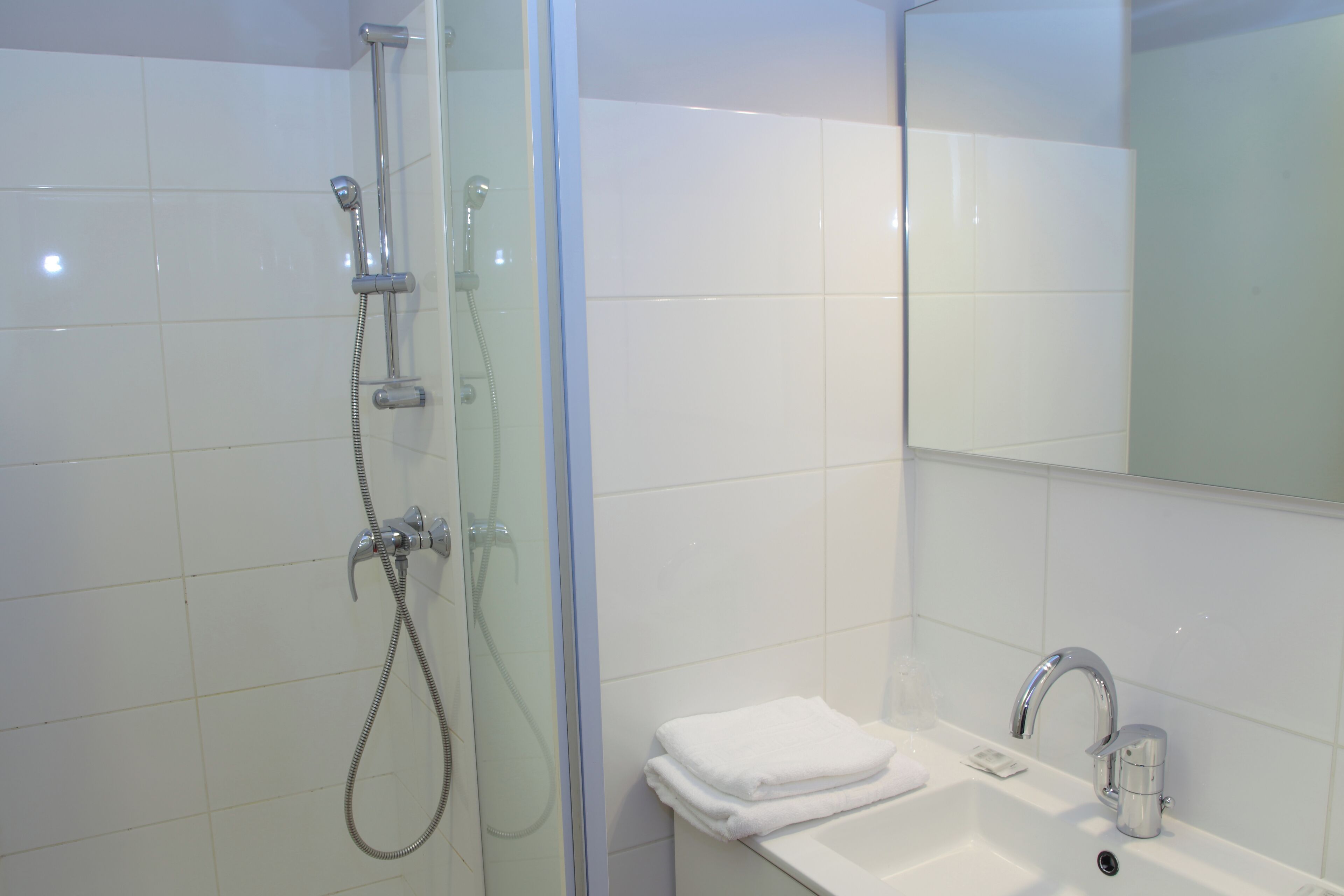 A bathroom with a glass-enclosed shower, a sink with a mirror, and a towel rack.