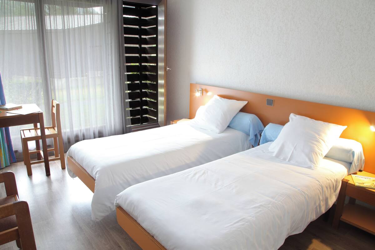 A hotel room with two beds, a desk, and a chair.