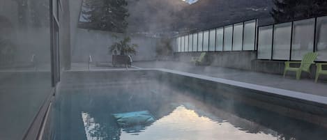 Una piscina con vistas despejadas a montañas al fondo, rodeada por un muro de cristal con sillas.