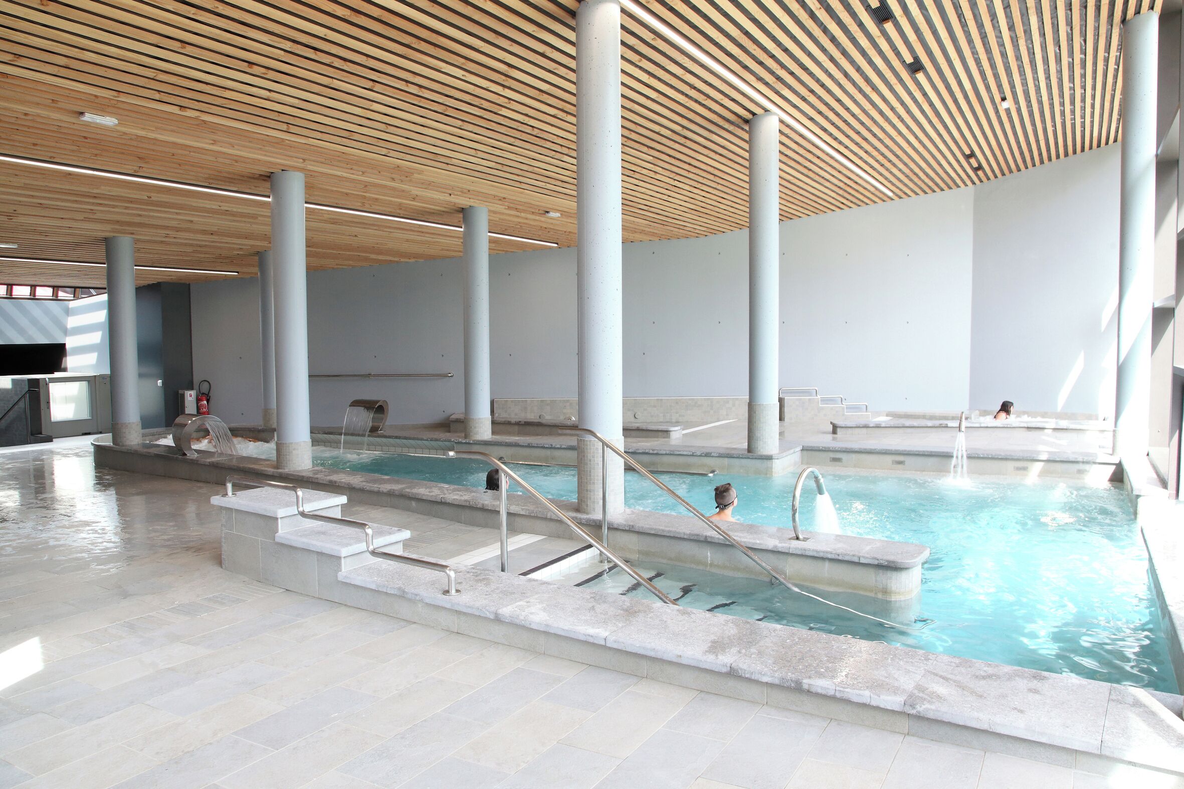 An indoor swimming pool with clear water, wooden ceiling, and steps leading into the pool.