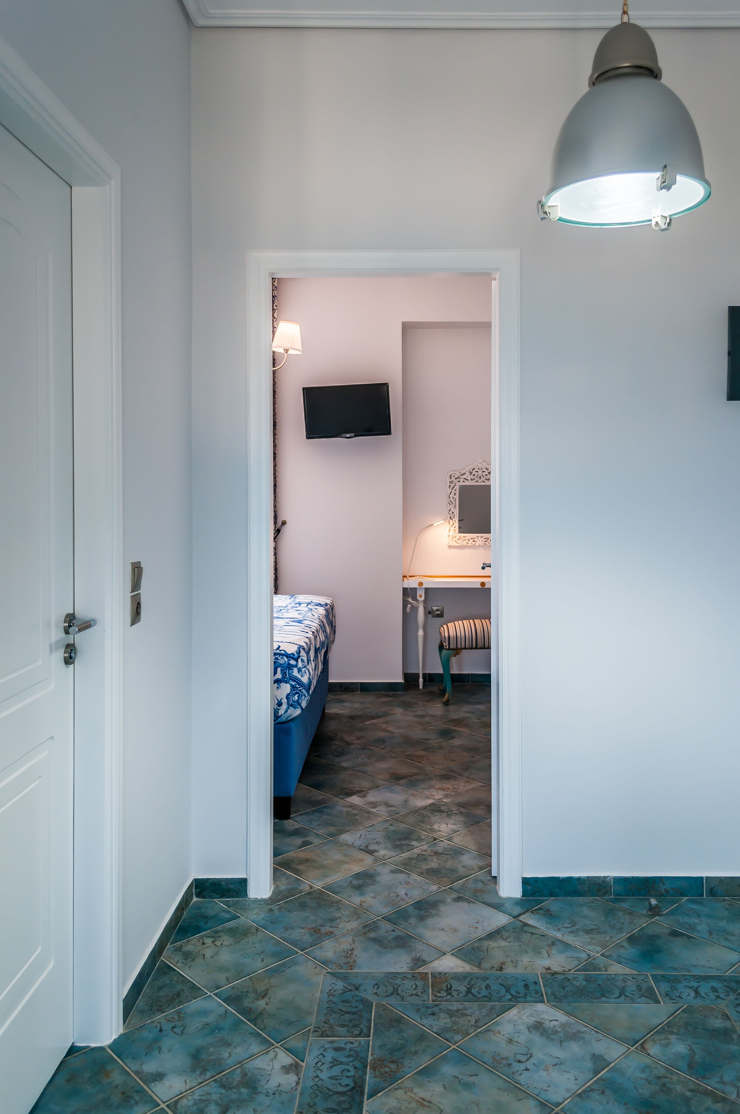 A narrow hallway leading to a bedroom with a bed, a bedside table, and a mirror.